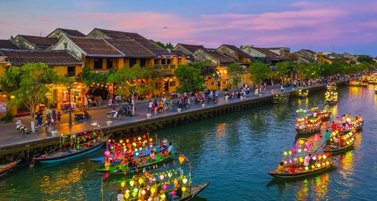 Von Laternen beleuchtete Boote auf einem Kanal in Hoi An bei farbenfrohem Sonnenuntergang