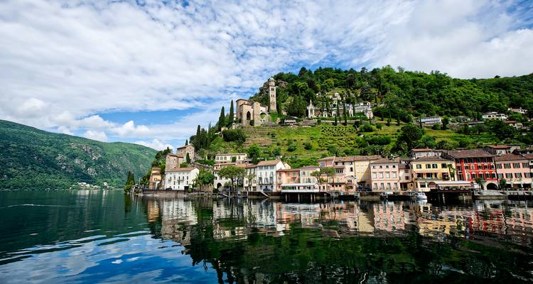 Farbenfrohes Dorf am Seeufer mit Ruinen am Hang, die sich in ruhigem Wasser spiegeln