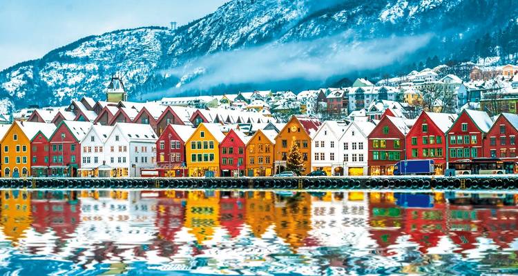 Ikonische Reihe von leuchtend bemalten Holzlagerhäusern im verschneiten Bergen, die sich perfekt im ruhigen Wasser spiegeln.