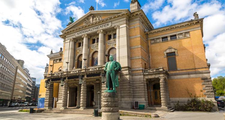 Historisches Nationaltheatergebäude in Oslo mit blauem Himmel und Statue davor.