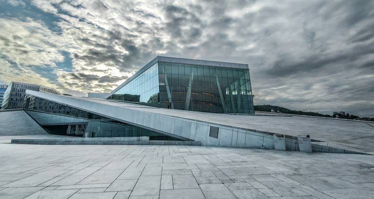 Modernes Glasopernhaus mit geneigten Marmorrampen unter einem dramatischen bewölkten Himmel