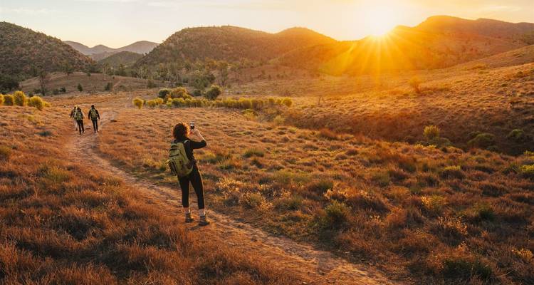 Wanderer gehen auf einem staubigen Pfad entlang und halten den feurigen Sonnenuntergang über den sanften Hügeln des Outbacks fest.