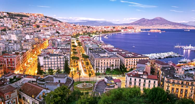 Vue au crépuscule sur la baie de Naples avec les lumières de la ville, la marina et le Mont-Vésuve en arrière-plan.