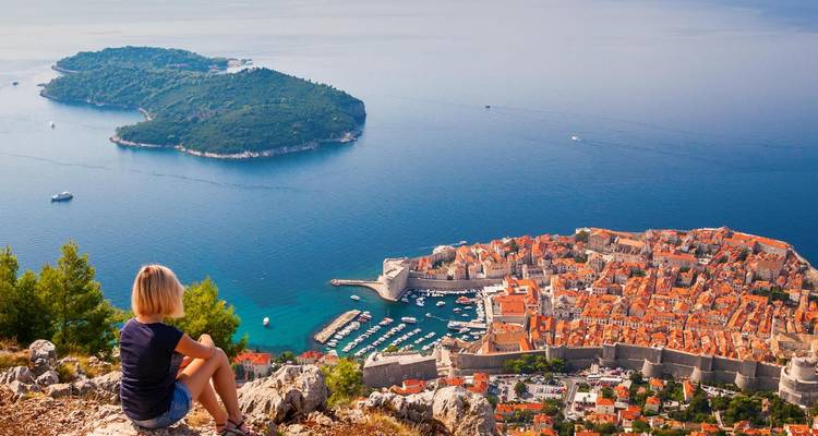 Frau, die auf einer Klippe sitzt und auf die Altstadt von Dubrovnik und die Adriainseln blickt.