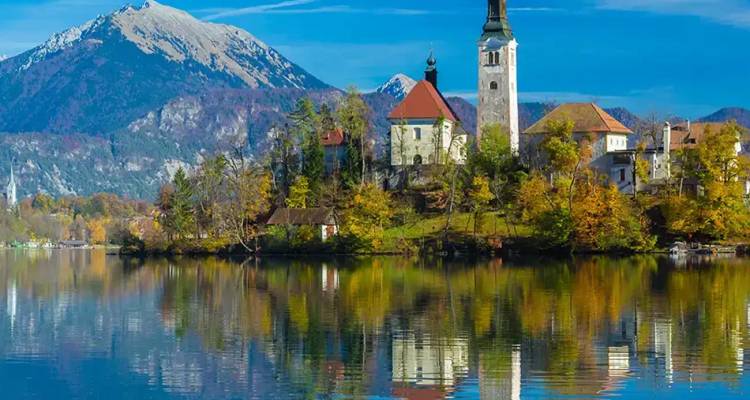 Église emblématique sur un îlot du lac de Bled se reflétant parfaitement dans l'eau calme avec les pics alpins en arrière-plan.