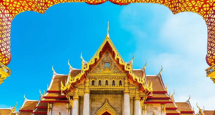 Een helder gekleurde Thaise tempel omlijst door een decoratieve boog tegen een levendige blauwe lucht.