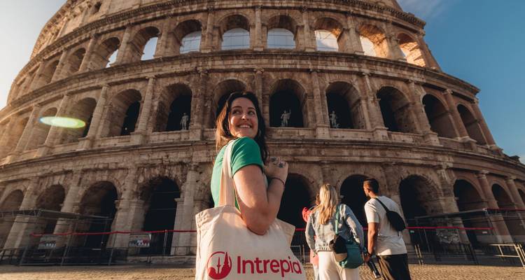 Un viajero sonríe frente al Coliseo de Roma llevando una bolsa Intrepid mientras la luz matutina ilumina los arcos.