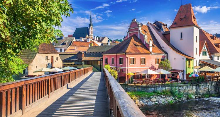 Casas coloridas y cafés a la orilla del río vistos desde un puente de madera en Cesky Krumlov en un día despejado.