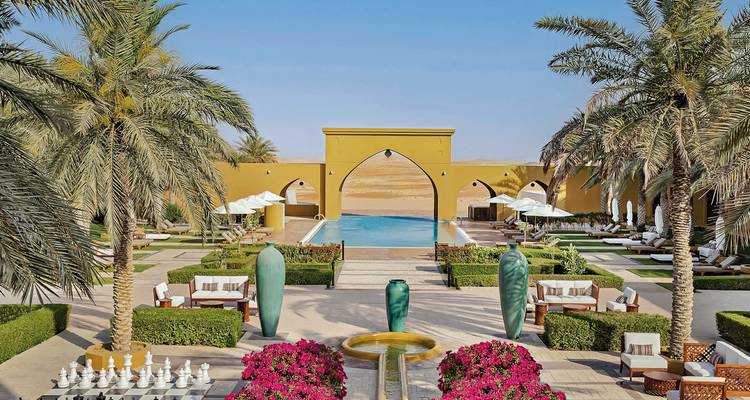 Eleganter Wüstenresort-Innenhof mit Palmen, Mosaikbrunnen und Infinity-Pool mit Blick auf goldene Dünen.