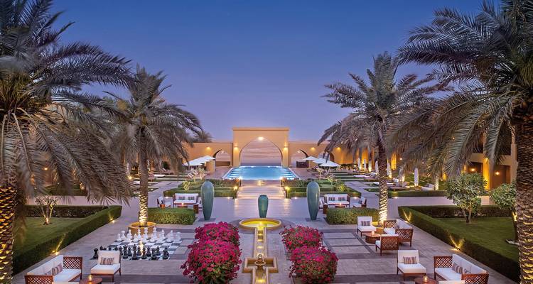 Derselbe luxuriöse Innenhof eines Wüstenresorts, der in der Dämmerung mit leuchtenden Laternen und einem tiefblauen Pool erleuchtet ist.