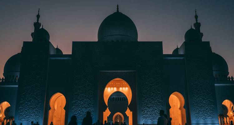Silhouette von Besuchern unter beleuchteten Bögen einer großen Moschee in der Dämmerung