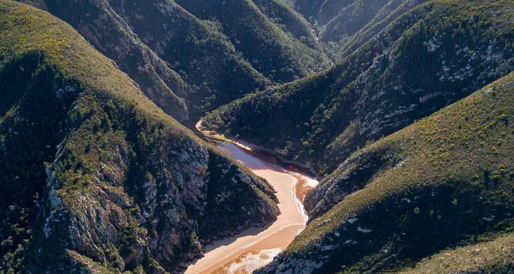 Vue aérienne d'une rivière sinueuse et sablonneuse traversant des vallées montagneuses escarpées et verdoyantes.