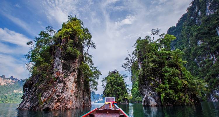Proue d'un bateau à moteur à longue queue en bois naviguant entre des formations calcaires spectaculaires sur une eau émeraude dans le parc national de Khao Sok.