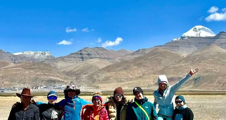 Groupe de randonneurs posant devant le Mont Kailash aux pics enneigés et les montagnes brunes et escarpées sous un ciel bleu profond.