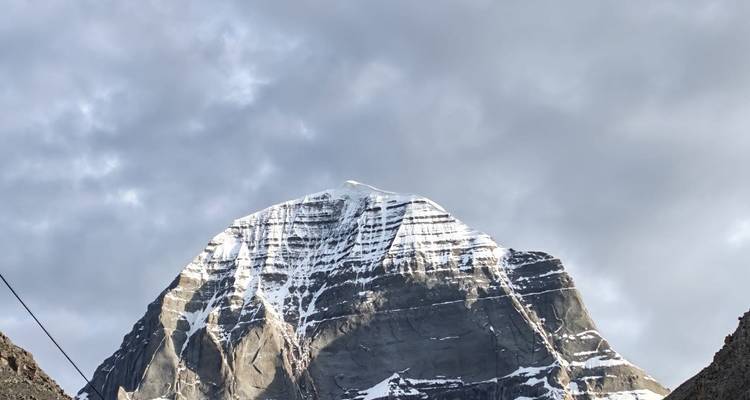 Forme pyramidale saupoudrée de neige du Mont Kailash sous un ciel gris morose.