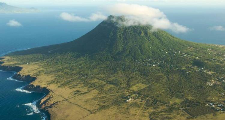 Pico volcánico solitario que se eleva desde las llanuras costeras con volutas de nube en la cumbre