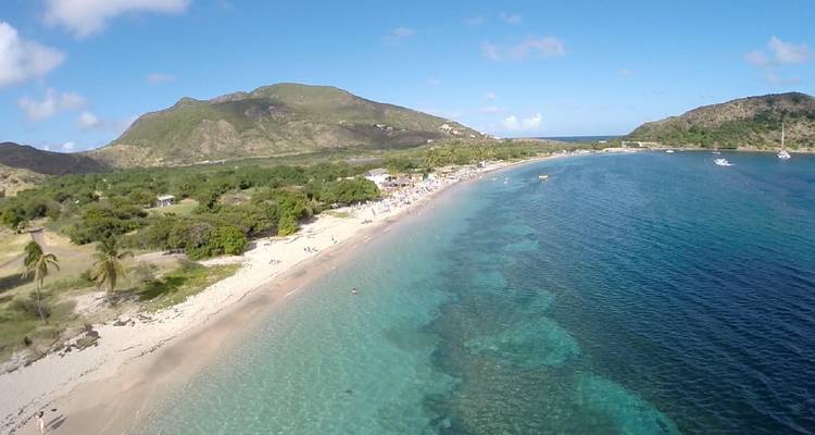 Drohnenaufnahme einer klaren, türkisfarbenen Bucht mit Sandstrand und grünen Hügeln