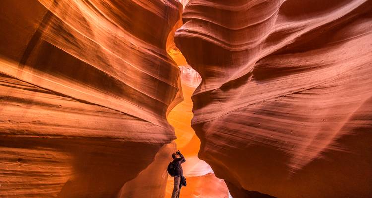 Photographe regardant vers le haut les parois étroites et sinueuses de grès du Canyon de l'Antilope éclairées par une lumière chaleureuse