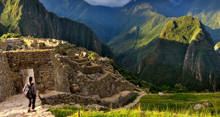 Viajero descendiendo por antiguos escalones de piedra en medio de las dramáticas ruinas Inca de Machu Picchu con exuberantes montañas alrededor.
