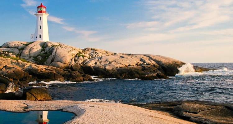 Weißer Leuchtturm auf zerklüfteten Granitfelsen neben einem dunkelblauen Meer während des goldenen Abendlichts