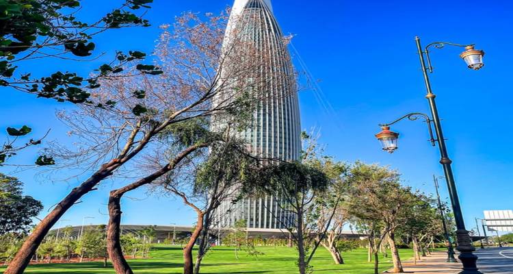 Gratte-ciel moderne et épuré s'élevant au-dessus d'espaces verts aménagés avec des candélabres décoratifs.