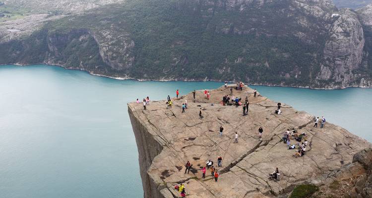 Des foules de randonneurs se tiennent au sommet de la falaise escarpée de Preikestolen surplombant les eaux turquoise du fjord