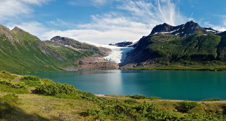 Lac glaciaire d'un turquoise éclatant sous des pics enneigés et des pentes verdoyantes lors d'une journée ensoleillée