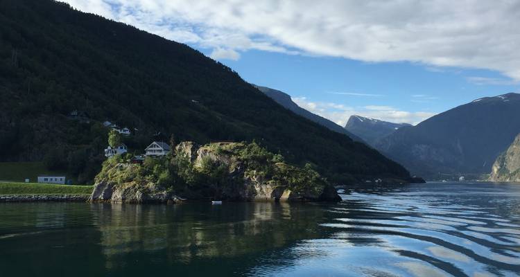 Petite île avec maisons située dans un fjord calme entouré de montagnes vertes abruptes