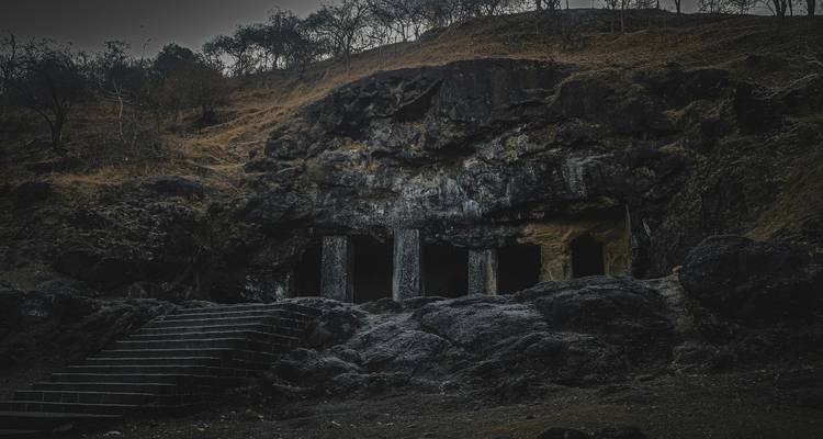 Schaduwen entree van oude in rots uitgehouwen grotten met stenen zuilen en ruw berglandschap daarboven