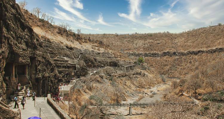 Bezoekers wandelen over het pad langs de klif met uitzicht op verschillende Ajanta grotelempels in een droog dal