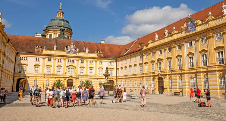 Cour de l'abbaye de Melk avec des facades baroques jaunes où un groupe de touristes se rassemble sous un ciel bleu éclatant.