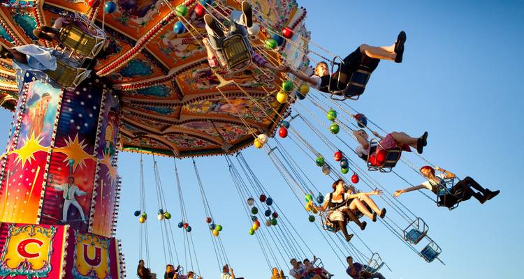 Los que buscan emociones se lanzan en un columpio colorido contra el cielo azul claro en una feria.