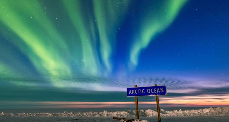 Nordlichter, die grün schimmernd über einem Schild der Arktischen See und einer gefrorenen, schneebedeckten Küstenlinie funkeln.