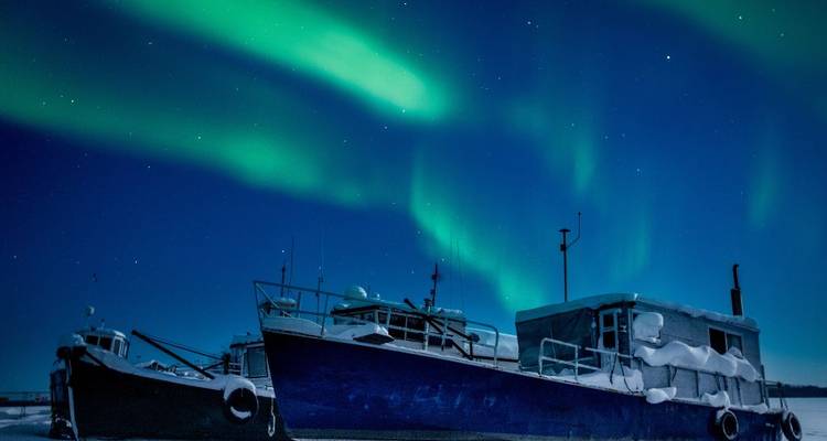 Vereiste Boote, die in einem gefrorenen Hafen nachts unter leuchtend grünen Nordlichtern vertäut sind.
