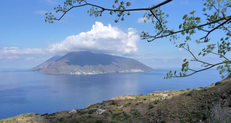 Distant volcanic island rising from calm blue sea under scattered clouds