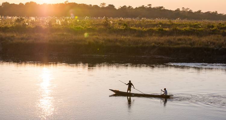 Silhouettenhafte Kanu mit zwei Paddlern gleitet über einen ruhigen Fluss hinweg, der die golden untergehende Sonne spiegelt.