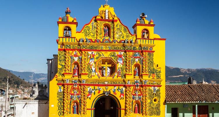 Fachada pintada de amarillo brillante de la iglesia San Andrés Xecul adornada con figuras vibrantes bajo cielos azules.