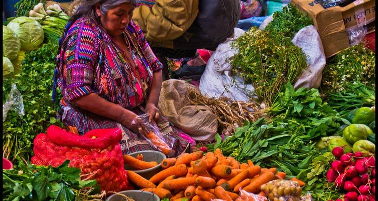 Una mujer indígena vende vegetales y hierbas vibrantes en un mercado guatemalteco lleno de vida.
