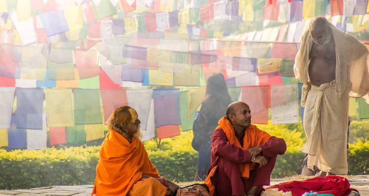 Los monjes envueltos en túnicas naranjas se sientan bajo banderas de oración multicolores ondulantes, creando una escena espiritual serena.