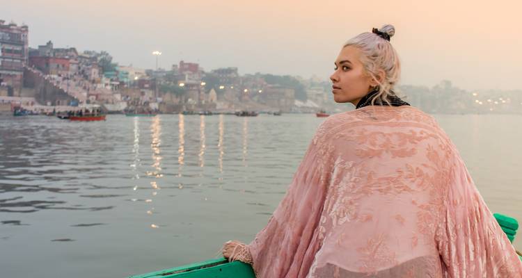 Mujer envuelta en un chal rosa contempla el río Ganges desde un bote al amanecer en Varanasi.