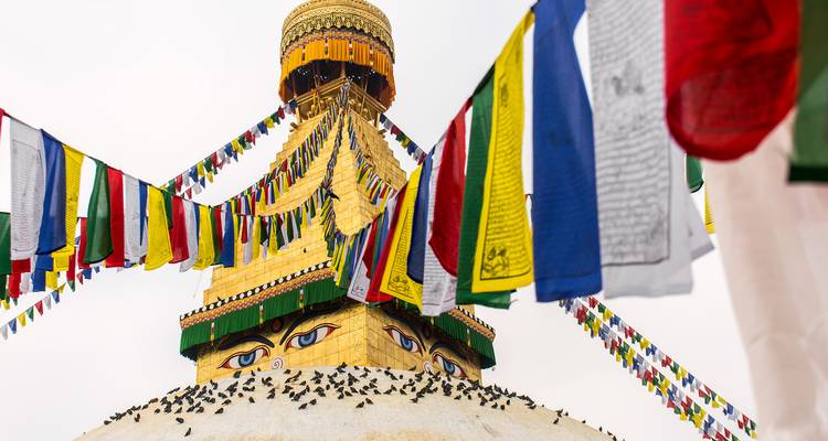 Estupa con cúpula dorada, los ojos del Buda pintados y hileras de banderas de oración multicolores contra un cielo pálido.