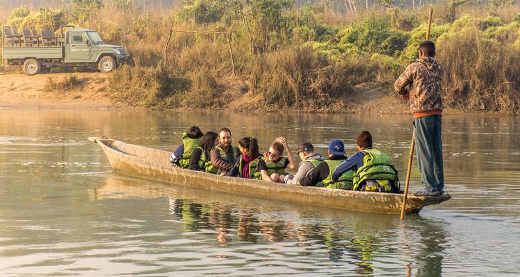 Turistas con chalecos salvavidas sentados en una canoa de madera delgada remando por un tranquilo río de la jungla al amanecer.