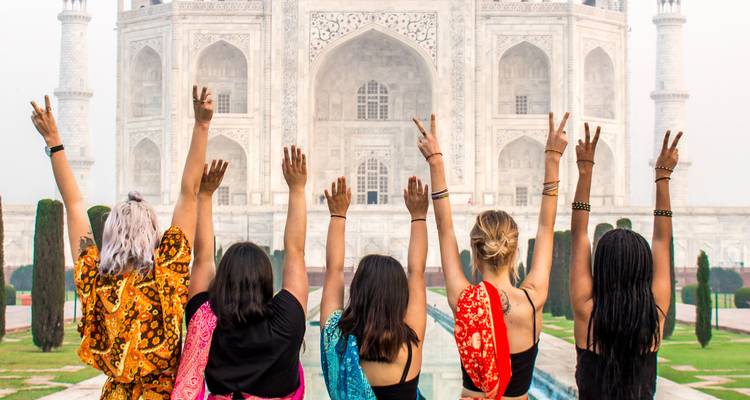 Cinco mujeres con saris coloridos levantanlos brazos hacia la fachada de mármol blanco del Taj Mahal.