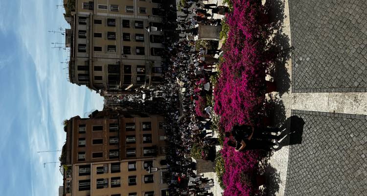 Menigten vullen de Spaanse Trappen en omringende straten, gezien vanaf een terras omzoomd met roze bloemen.