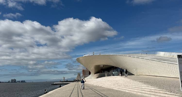 Edificio blanco y moderno del museo MAAT con curvas suaves a lo largo del paseo fluvial bajo un cielo azul parcialmente nublado.