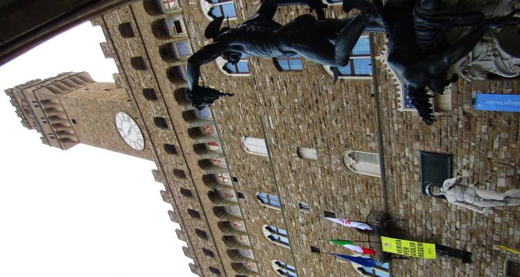 Vue ascendante de la tour du Palazzo Vecchio avec des statues au premier plan et des drapeaux sur la façade