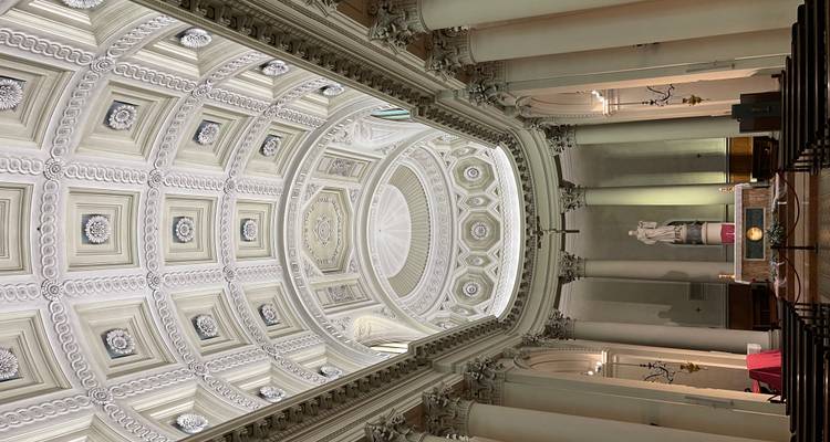 Intérieur d'une église néoclassique avec des colonnes majestueuses, un plafond en dôme à motifs et un autel en statue de marbre central