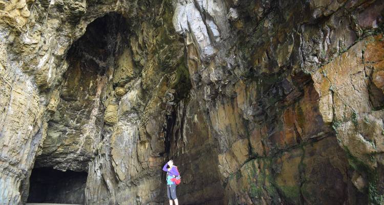 Un voyageur contemple les imposantes parois rocheuses texturées d'une immense grotte marine.