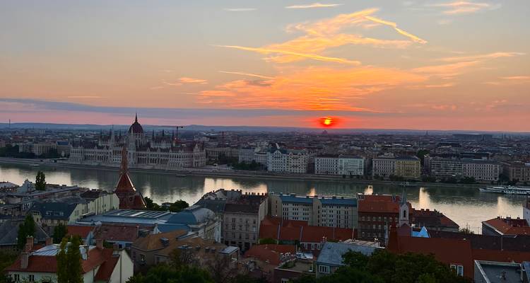 Die Farben eines glutroten Sonnenuntergangs spiegeln sich in der Donau wider, mit dem Parlamentsgebäude von Budapest und den Dächern der Stadt darunter.