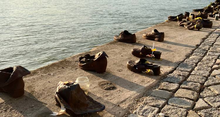 Rostige Eisenschuhe des Donauufer-Denkmals, beleuchtet durch warmes goldenes Licht der golden hour neben dem Fluss.